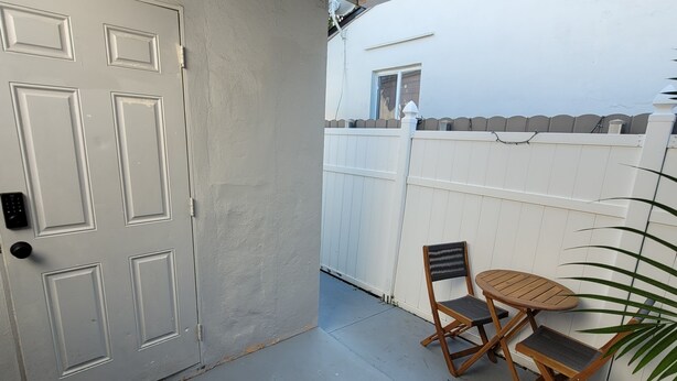 Un patio couvert avec une porte blanche, une petite table et deux chaises, et une clôture blanche en arrière-plan.