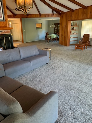 A spacious living room with a grey sectional sofa, a small round coffee table, and a wooden bookshelf.