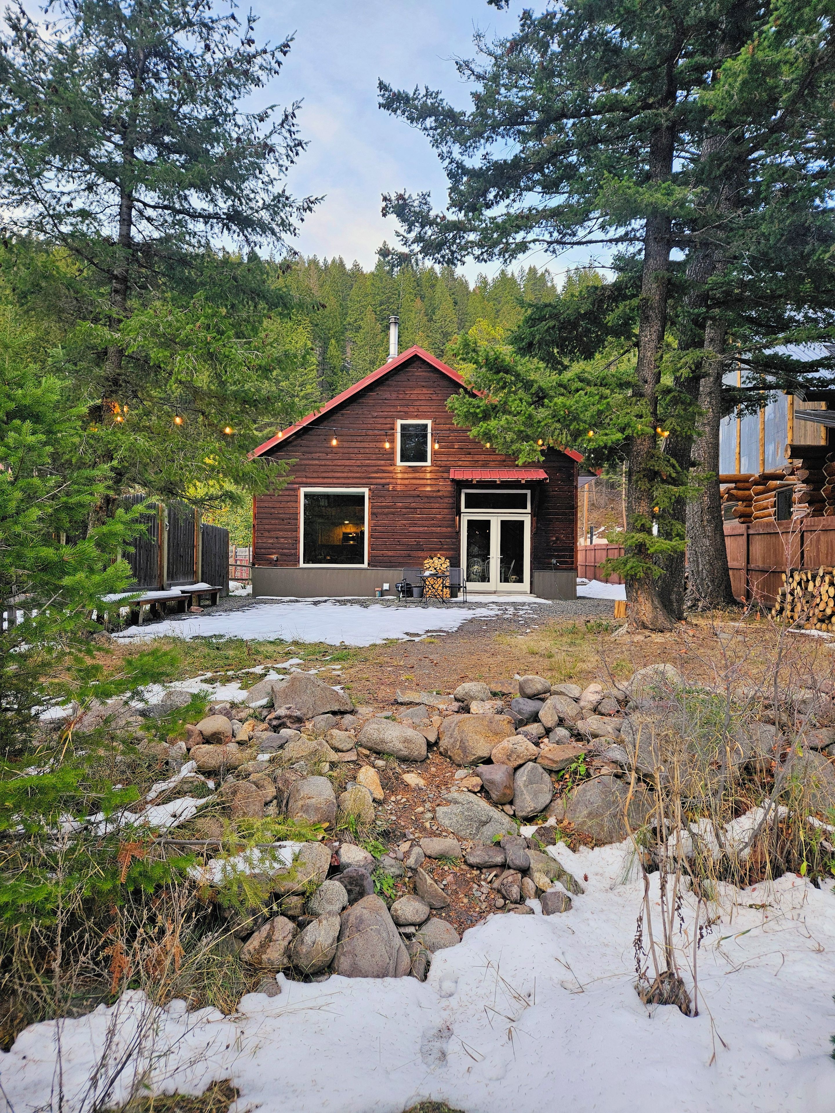 Une cabane rustique avec un toit rouge, entourée d’un paysage naturel composé de rochers et d’arbres.