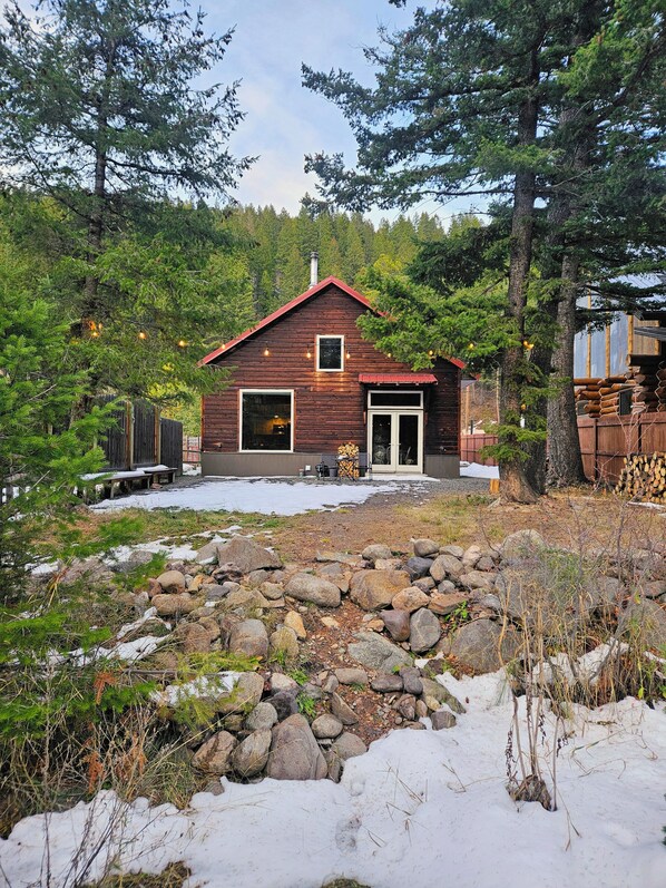 A rustic cabin with a red roof, surrounded by a natural landscape with rocks and trees.