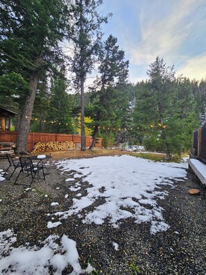 A backyard with a gravel patio, a wooden deck, and a stack of firewood.