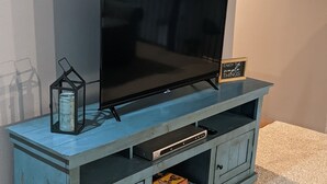 Sininen viihdekeskus, jossa on litteänäyttöinen televisio, pieni hylly, jossa on kyltti, ja muutama lautapeli.