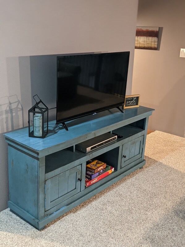 Un mueble azul para entretenimiento con un televisor de pantalla plana, un estante con un letrero y algunos juegos de mesa.