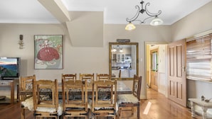 A dining area with wooden chairs and a table, a television, and a painting on the wall. - Welcome to our charming, 2-level house just 5 min walk to 3 Sisters, Echo Point! (Katoomba)