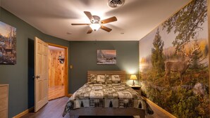 A bedroom with a wooden bed, a ceiling fan, a nightstand with a lamp, and a large deer mural on the wall. - Spruce Haven - 5 br home on 53 acres with pond (Meshoppen)
