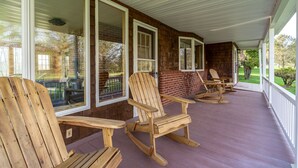 A covered porch with wooden rocking chairs and a brick wall. - Spruce Haven - 5 br home on 53 acres with pond (Meshoppen)