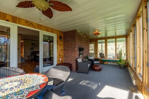 A covered patio with wicker furniture, a brick fireplace, and large windows.