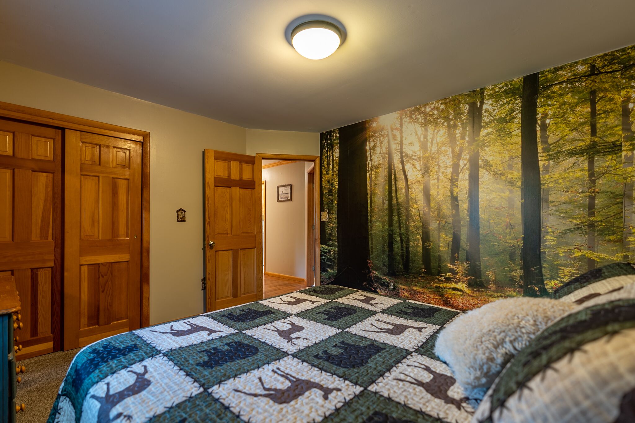 Un dormitorio con colcha acolchada de motivos de ciervos, puertas de madera y un mural temático de bosque.