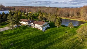 A large house with a covered porch, a pond, and a well-maintained lawn. - Spruce Haven - 5 br home on 53 acres with pond (Meshoppen)