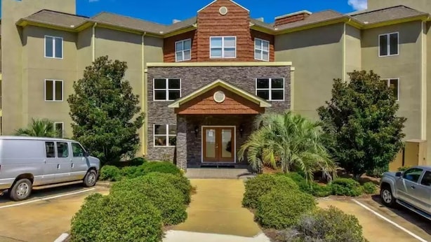 A multi-story building with a central entrance, surrounded by greenery and parked vehicles. - Lovely Lake Condo with BOAT SLIP and Pool (Alexander City)