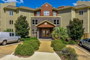 A multi-story building with a central entrance, surrounded by greenery and parked vehicles. - Lovely Lake Condo with BOAT SLIP and Pool (Alexander City)