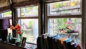 Une pièce avec une fenêtre donnant sur un jardin, une bibliothèque remplie de livres et un vase de fleurs posé sur le rebord de la fenêtre.