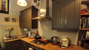 Une cuisine équipée d’une cuisinière, d’un four et de divers appareils électroménagers. On y trouve un évier et un plan de travail sur lequel sont posés différents objets.