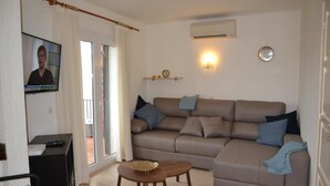 A living room with a sofa, a coffee table, a TV, and a wall-mounted air conditioner. - Casa Gaudir - L'Estartit, Torre Vella (Estartit (L´))