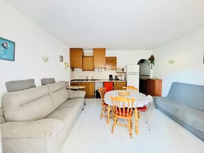 A compact living space with a sofa, dining table, chairs, and a kitchenette.