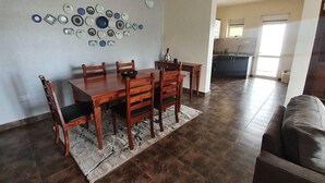 Un comedor con una mesa y sillas de madera, un adorno en la pared y una cocina al fondo.