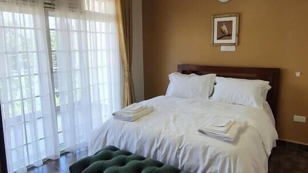 Un dormitorio con una cama, un banco tapizado de color verde, un ventilador de techo y una ventana con cortinas.