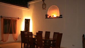 Un coin repas comprenant une table ronde et six chaises, une étagère décorative fixée au mur et une lanterne suspendue.