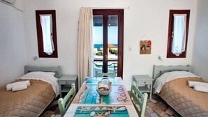 Een kamer met twee bedden, een tafel met een bord waarop 'Relax' staat, uitzicht op zee door een raam en een klein balkon.