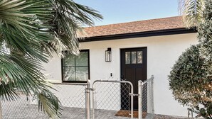 A white building with a black door, a chain-link fence, and a palm tree. - Cozy Desert Remodeled 2-bedroom Home (Gilbert)