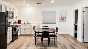 A modern kitchen with white cabinets, a dining table with chairs, a refrigerator, a microwave, and a stove. - Cozy Desert Remodeled 2-bedroom Home (Gilbert)