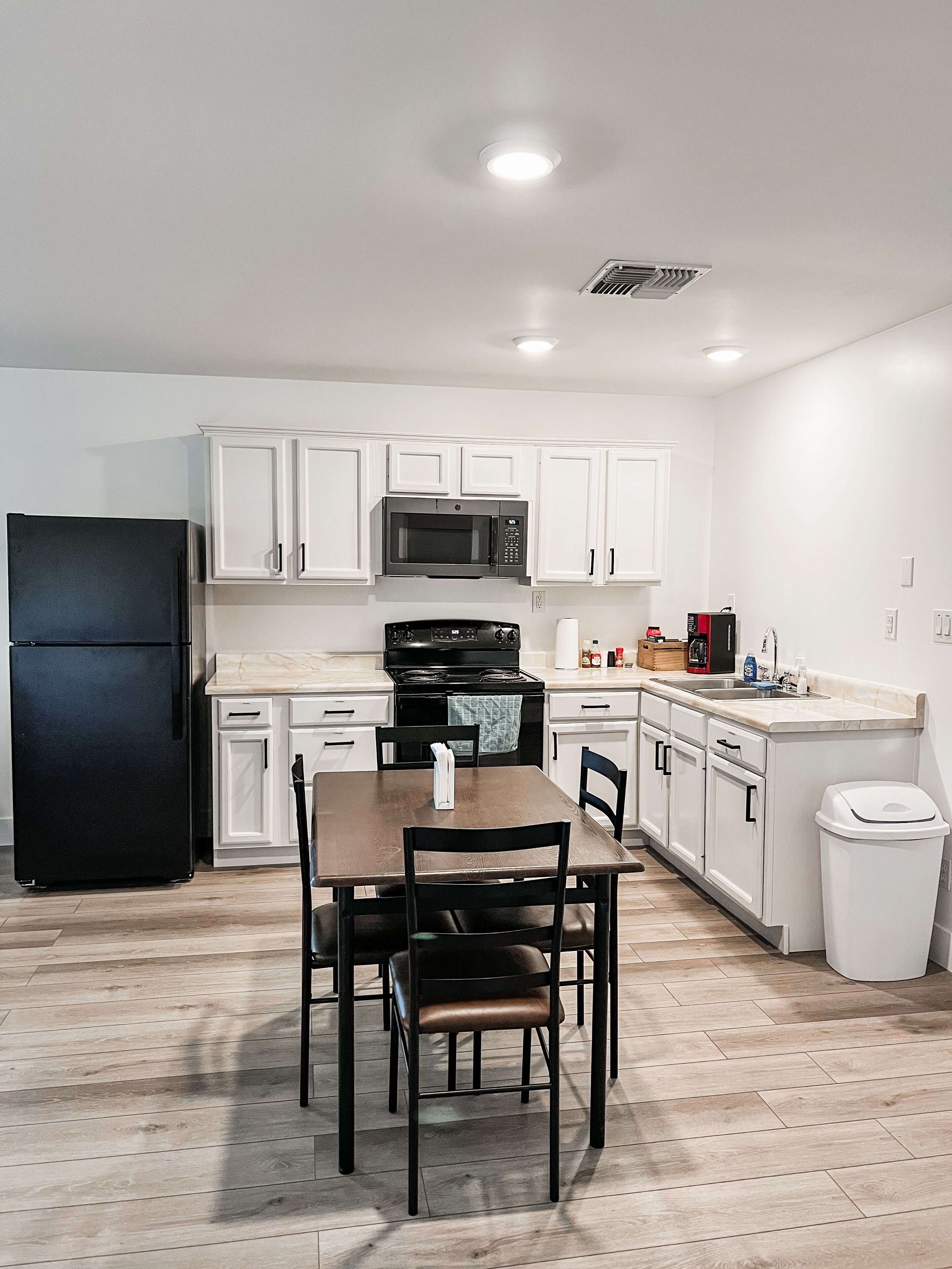 A compact kitchen with white cabinets, a black refrigerator, a microwave, a stove, and a dining table with chairs.