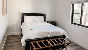 A bedroom with a bed, a ceiling fan, a nightstand, a window, and a wooden bench. - Cozy Desert Remodeled 2-bedroom Home (Gilbert)