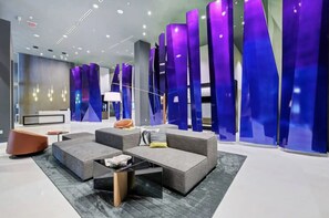 A modern lobby with a seating area featuring sofas and a coffee table, a reception desk, and a decorative wall with vertical elements.