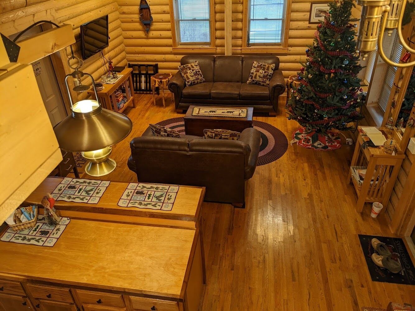 A cozy log cabin interior with a wooden dining table, a sofa, and a Christmas tree.
