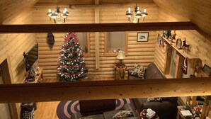 Et interiør af en hytte med bjælkevægge, en juletræ og en loftsvifte.