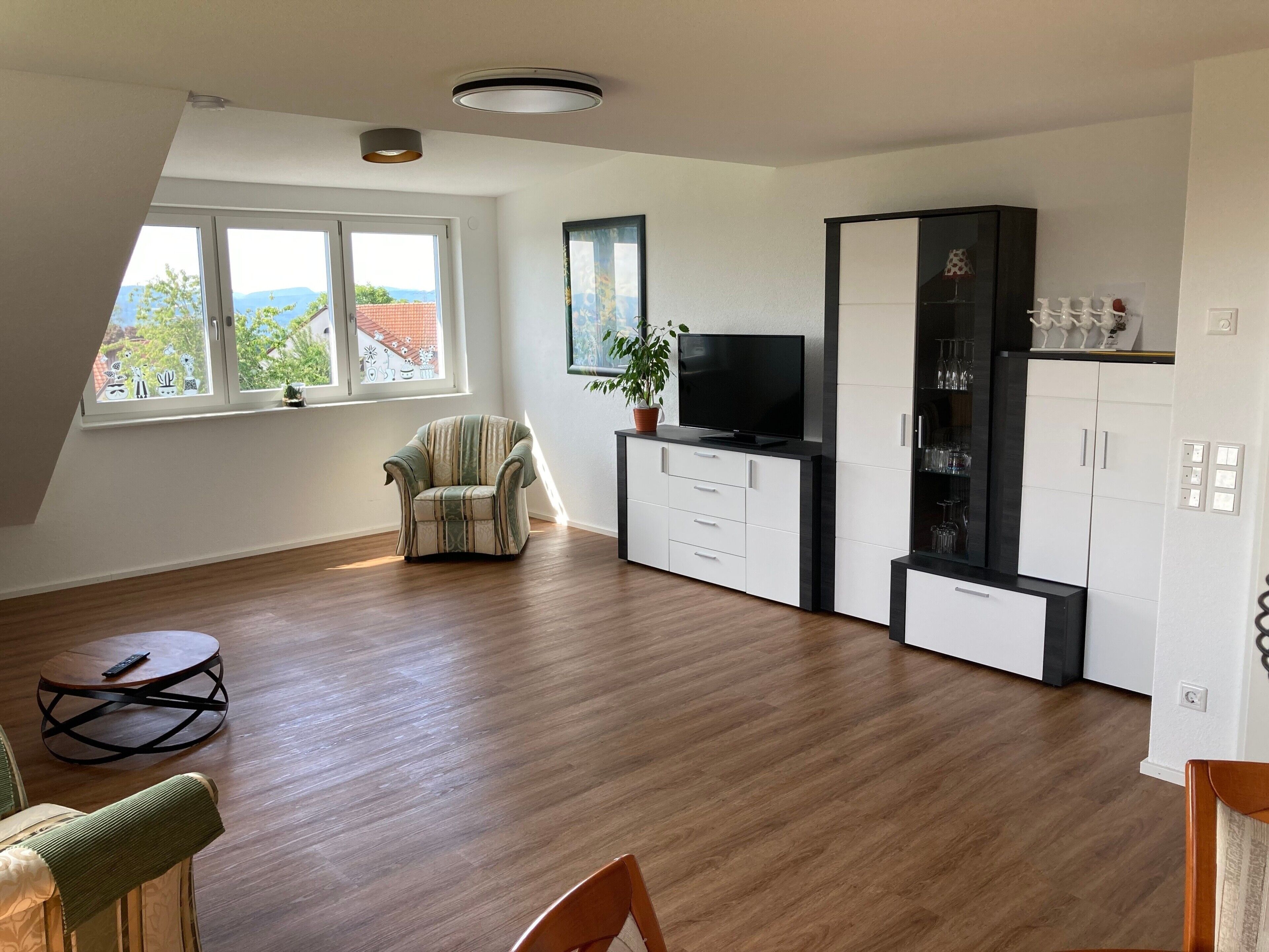 Una sala de estar moderna con piso de madera, un sillón a rayas, un televisor sobre un mueble bajo, y un comedor con una mesa redonda.