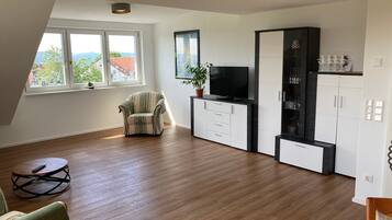 Una sala de estar moderna con piso de madera, un sillón a rayas, un televisor sobre un mueble bajo, y un comedor con una mesa redonda.