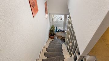 Eine Treppe mit Handlauf, ein Blumentopf und Blick auf einen Balkon mit weißem Geländer.