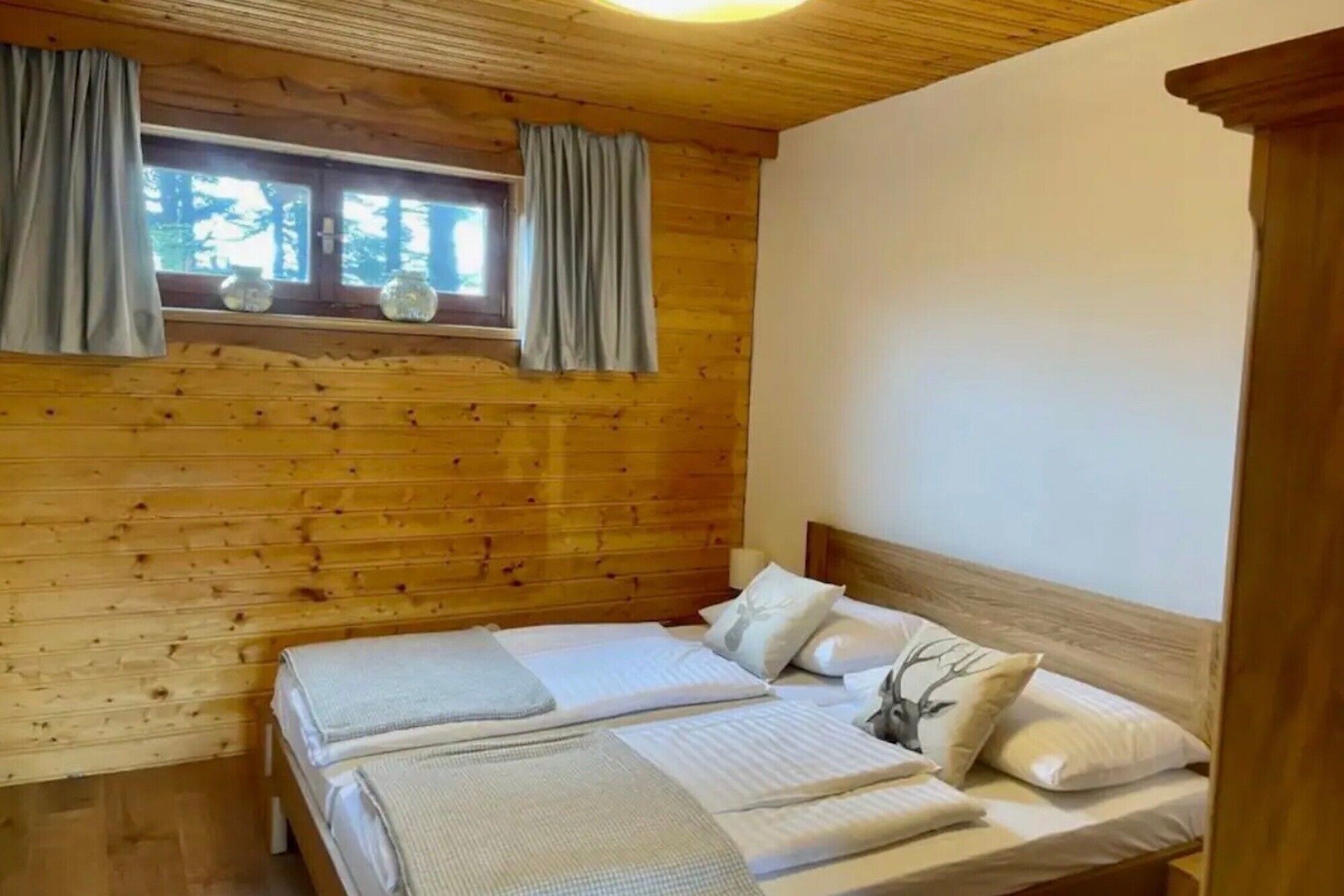 Ein Schlafzimmer in einer Holzhütte mit zwei Betten, einem Fenster mit Vorhängen und einer Holzbalkendecke.