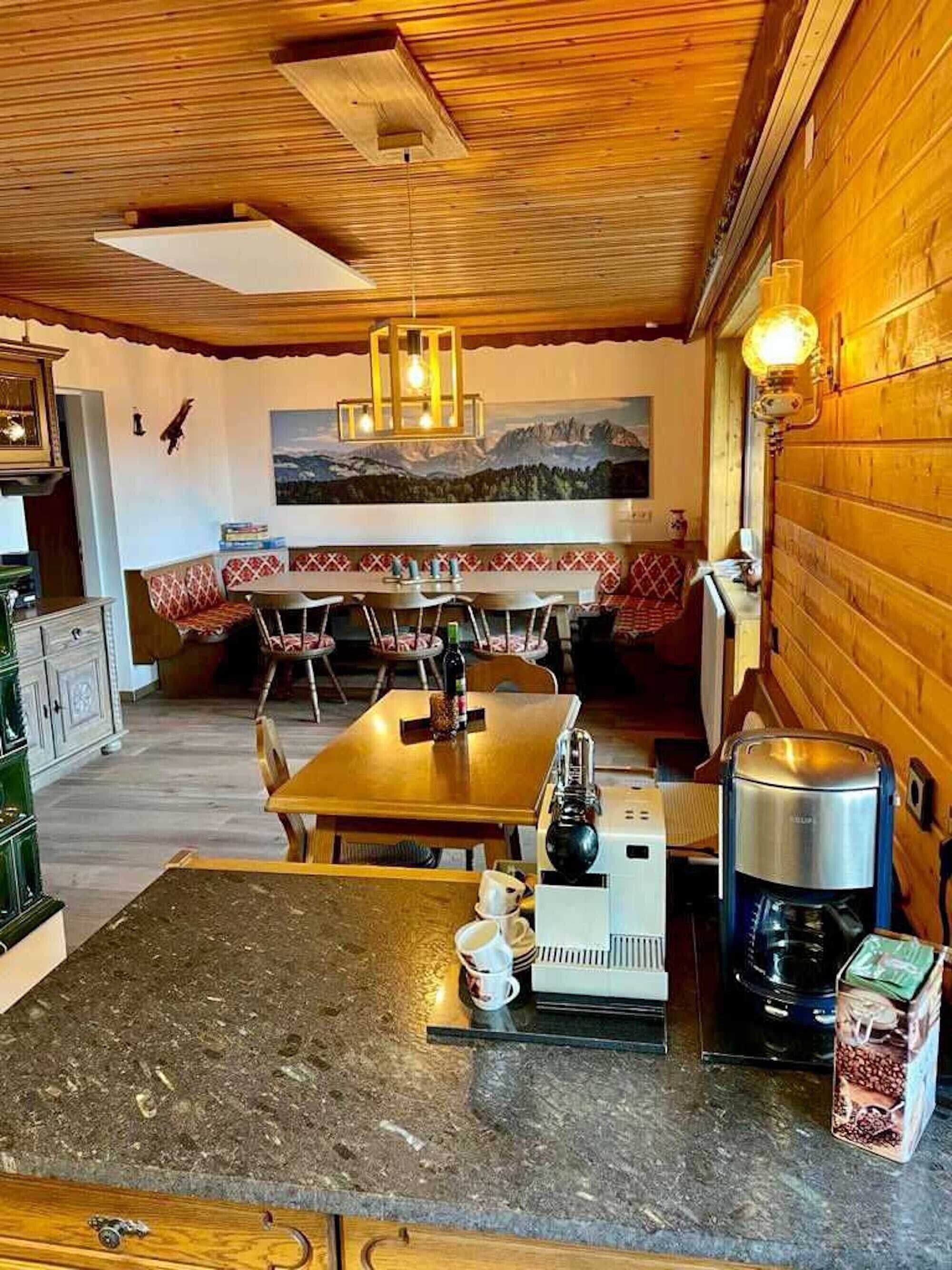 Une cuisine chaleureuse avec une table en bois, des tabourets de bar, une machine à café et un tableau accroché au mur.