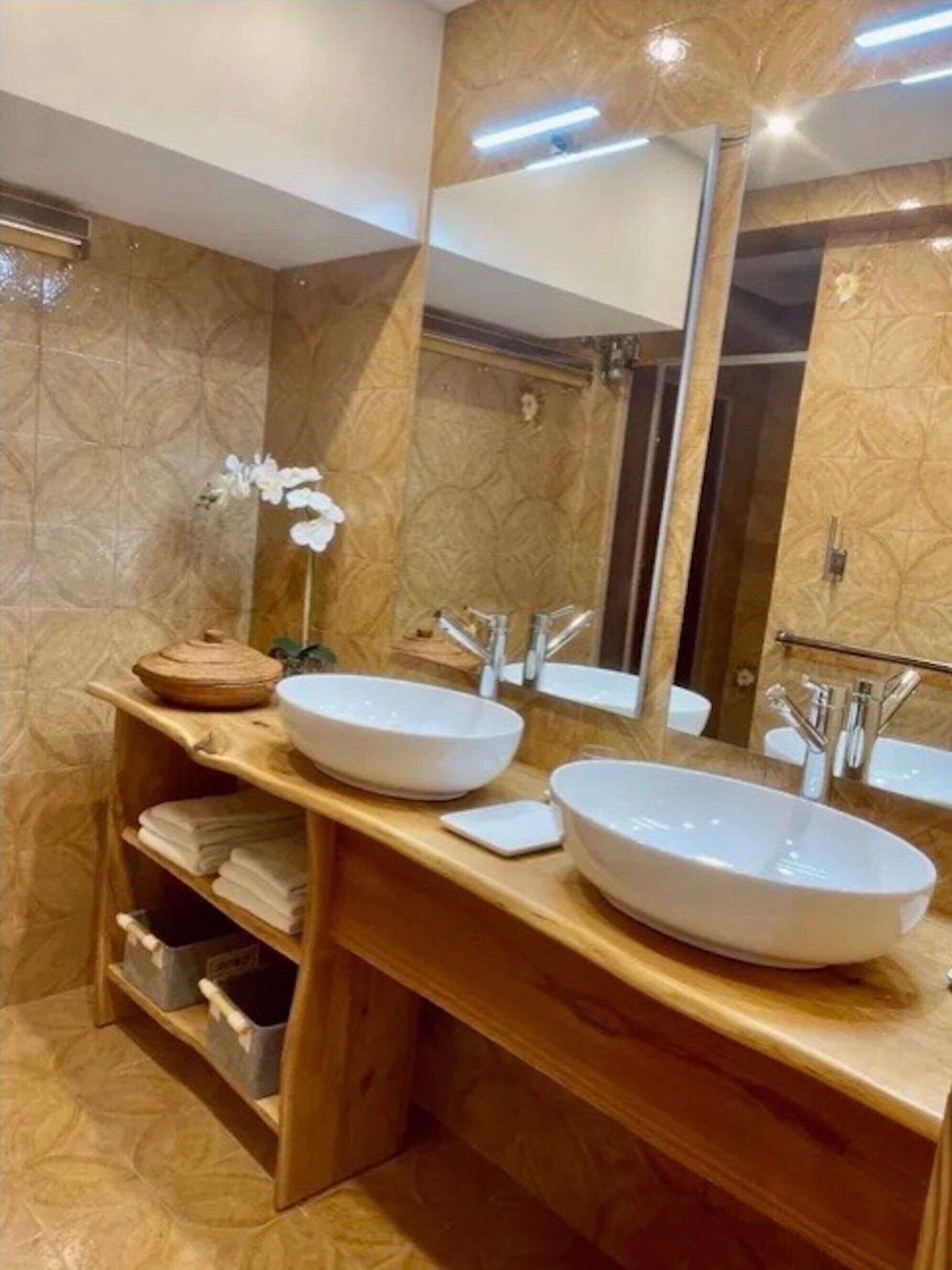 A bathroom with two large white sinks, a wooden vanity, a mirror, and a single white orchid.