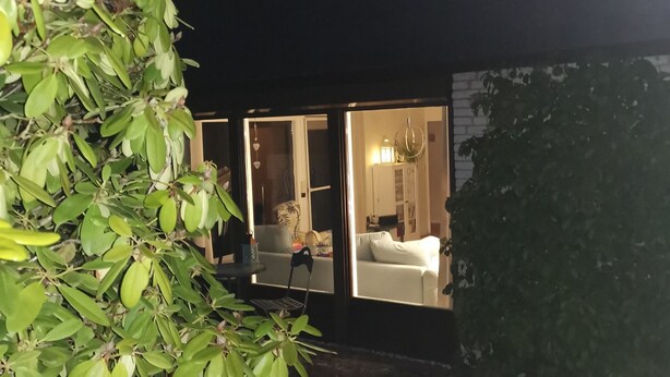Una casa amb façana fosca, grans finestres i mobles interiors a la vista.