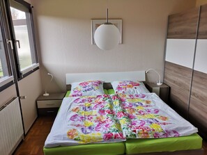 Une chambre à coucher comprenant un lit, des tables de chevet, une lampe suspendue, un radiateur et une fenêtre.