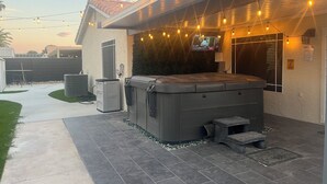 A backyard with a hot tub, outdoor seating, and string lights.