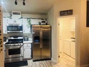 Een keuken met roestvrijstalen apparatuur, een magnetron, oven en een koelkast. Op de muur hangt een bordje met de tekst 'The Laundry Room'.
