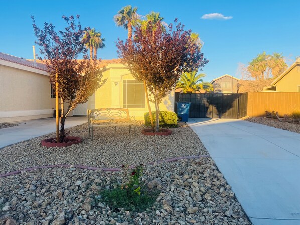 A residential area with a paved driveway, a bench, and a small garden with rocks and plants.