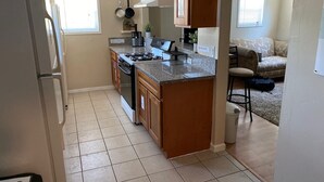 Una cocina con armarios de madera, una estufa y un refrigerador. Hay una zona de comedor con un sofá y una silla.