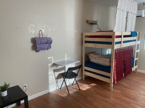 A room with a bunk bed, a desk with a chair, a small table with a plant, and a wall-mounted shelf with towels. - WHOLE Family - Barrette - back - Hostel (Sacramento)