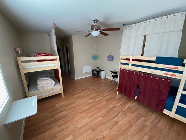 A room with bunk beds, a ceiling fan, a small table, and a window.