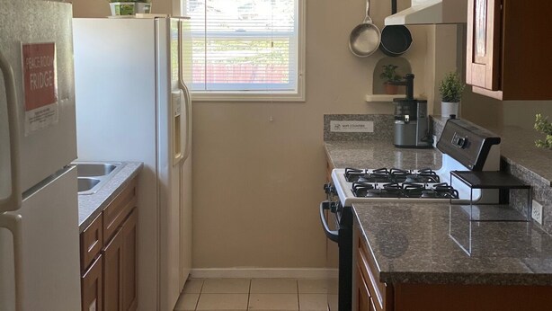Cocina compacta con refrigerador, estufa, lavaplatos y ventana con persianas.