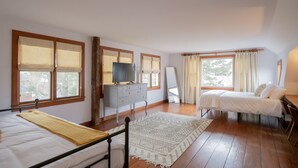 Un dormitorio con dos camas, un aparador, un televisor y un ventanal amplio.