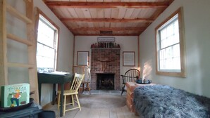 Une pièce chaleureuse avec une cheminée en briques, des poutres en bois au plafond, un bureau avec une chaise et un banc recouvert de fourrure.