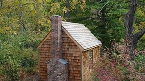 Une petite cabane en bois, dotée d’une cheminée, entourée d’arbres et de feuillage.