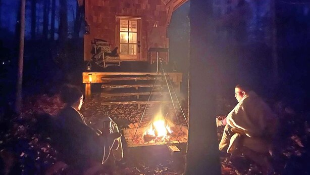 Une cabane avec une façade en bois, une véranda et un foyer à l’extérieur.