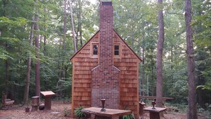Une cabane en bois avec une cheminée en briques, entourée d’arbres au cœur d’une forêt.